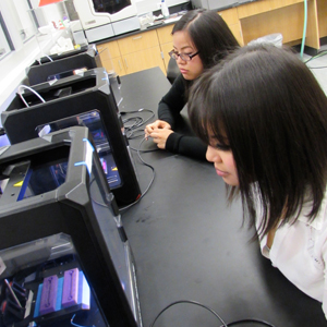 Students Michelle Le and Tu Le looking at the molds for their devices inside 3D printers